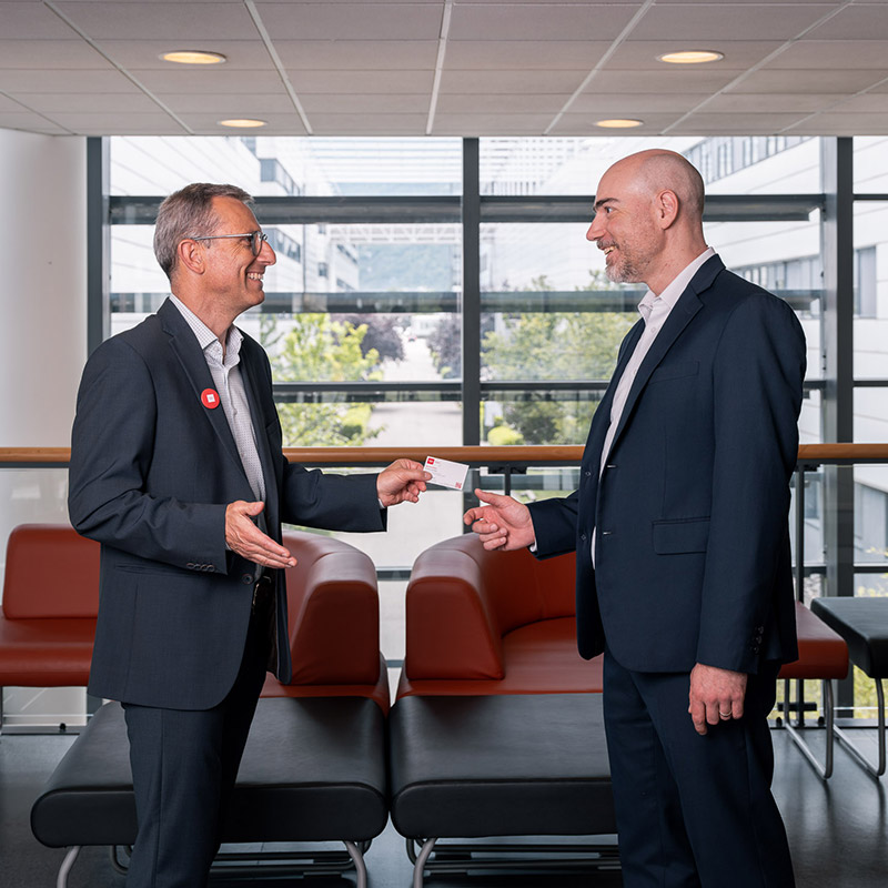 two smiling men, in suits, exchange a business card